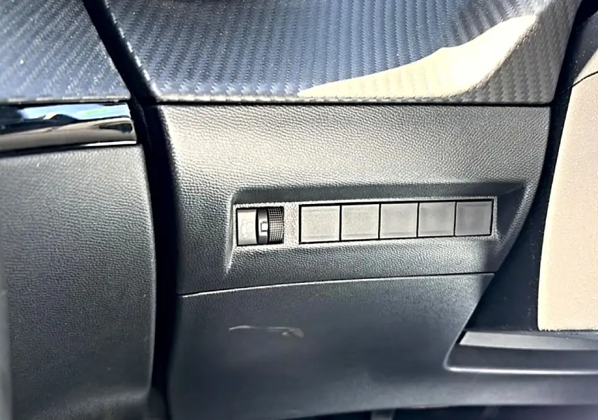 Détail intérieur côté gauche du tableau de bord noir avec commande de réglage des phares du Peugeot 2008 gris 2025.