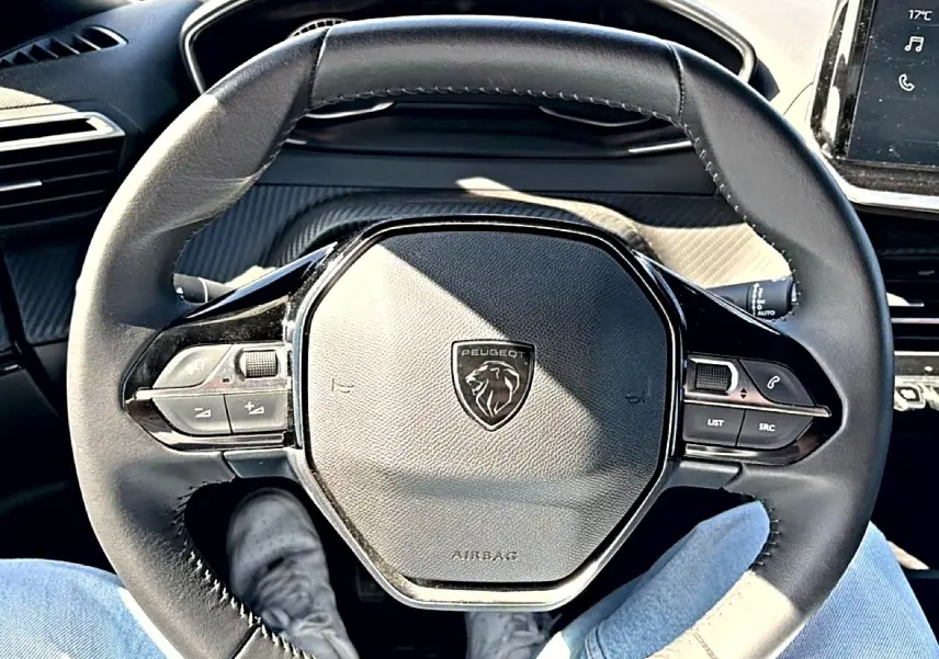 Vue rapprochée du volant multifonction noir du Peugeot 2008 1.2 100 style avec logo lion central, intérieur gris.