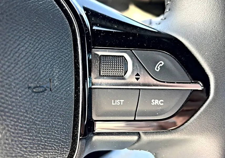Gros plan sur les commandes gauche du volant noir du Peugeot 2008 gris, boutons LIST et SRC visibles.