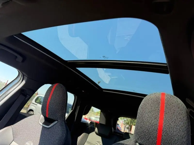 Vue intérieure du MINI Countryman argenté 2025, toit panoramique ouvert et sièges avant avec bande rouge centrale.