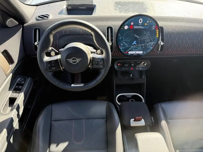 Vue intérieure avant du tableau de bord et volant noir du MINI Countryman argenté avec écran tactile rond affichant la navigation.