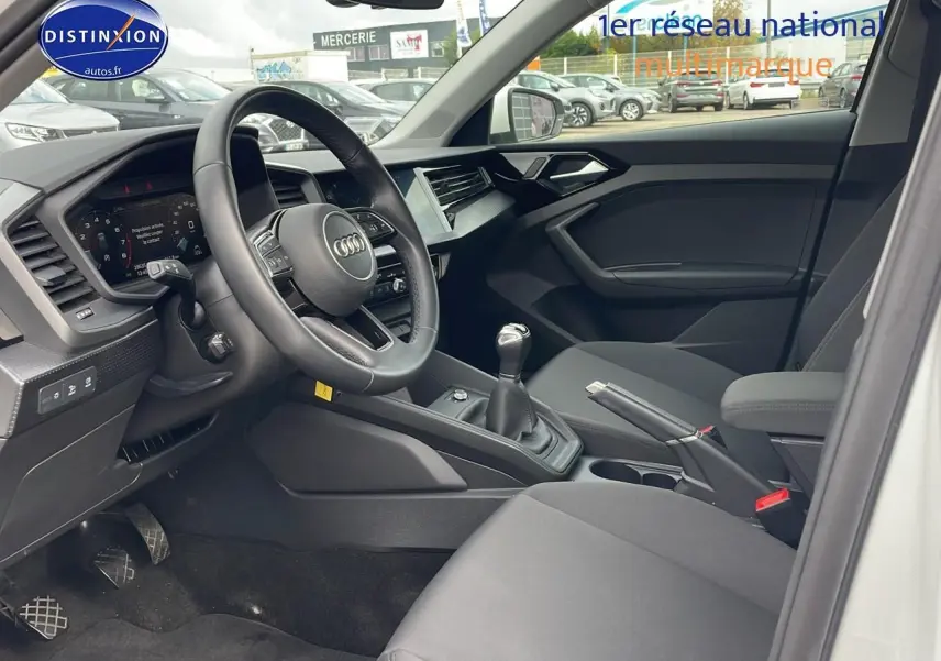 Intérieur de l'Audi A1 Sportback blanc 2022 vu côté conducteur, volant cuir sport et boîte manuelle visible.