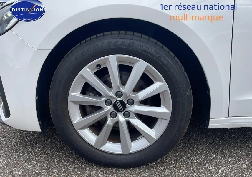 Gros plan sur la roue avant gauche blanche d'une Audi A1 Sportback 30 TFSI avec jante alu 16 pouces et logo Audi central.