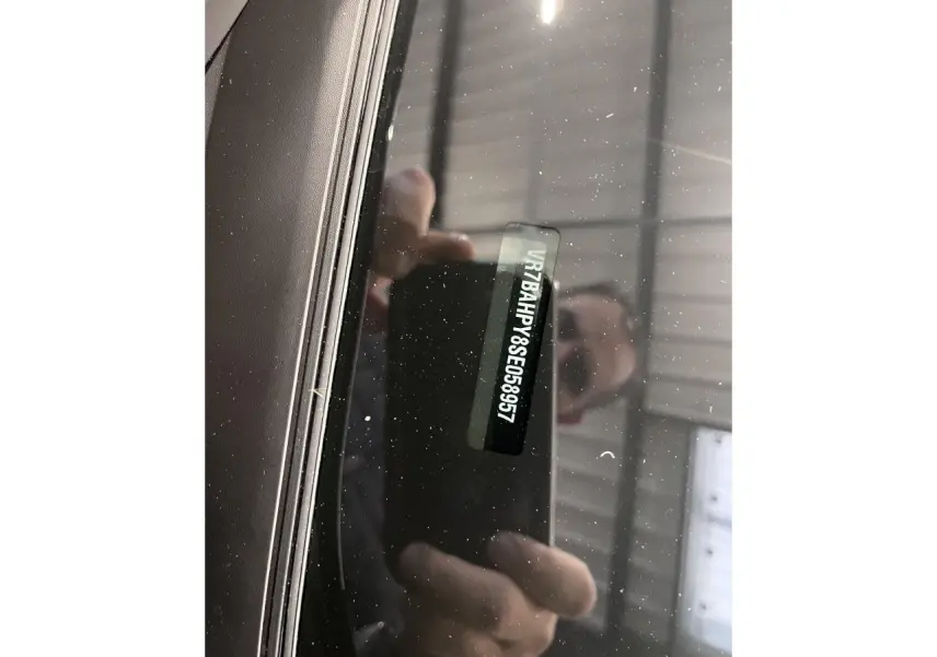 Vue rapprochée du pare-brise avant d'une Citroën C4 noire métallisée, montrant le numéro VIN visible à travers le verre.