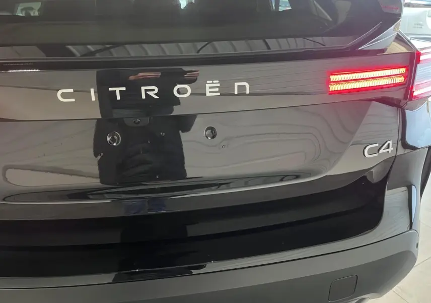 Vue arrière rapprochée de la Citroën C4 noire métallisée avec feux arrière LED allumés et logo distinctif.