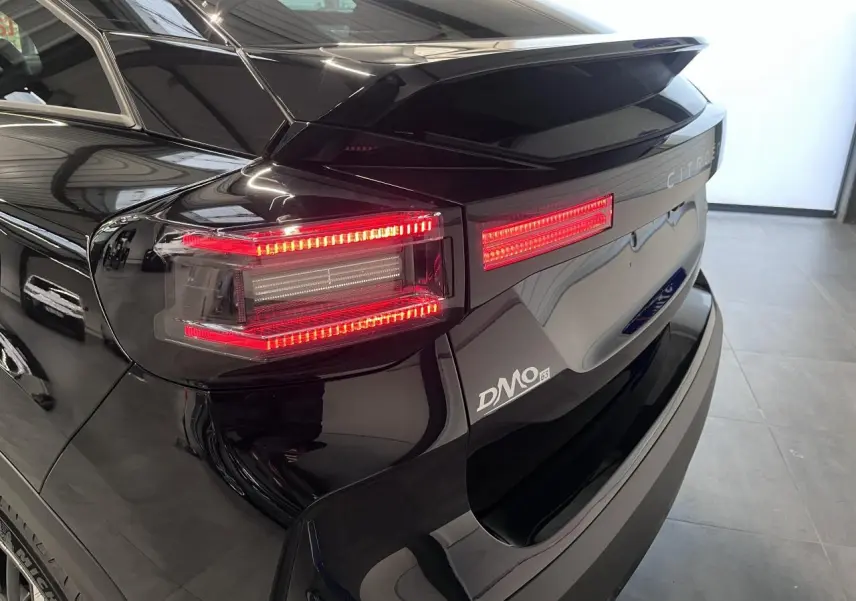 Vue arrière droite d'une Citroën C4 noire métal avec feux LED allumés et logo DMO visible sur le coffre.