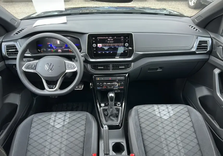 Vue intérieure frontale du Volkswagen T-Cross TSI 116 DSG7 R-Line 2025, sièges tissu gris à motifs géométriques et tableau de bord digital.