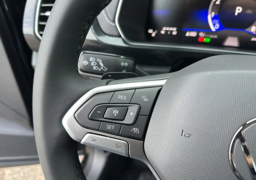 Gros plan sur le volant cuir noir du Volkswagen T-Cross 2025, avec commandes multifonctions et tableau de bord digital.