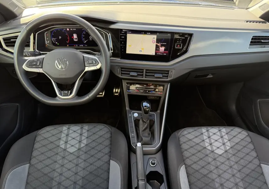 Vue intérieure avant du Volkswagen Taigo 2025 montrant le volant multifonctions, l'écran tactile et la console centrale noire.