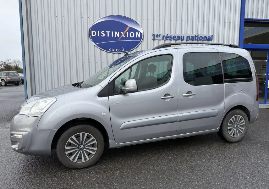 Vue de profil côté gauche d'un Peugeot Partner Tepee gris 2018 garé devant un bâtiment avec logo Distinxion.