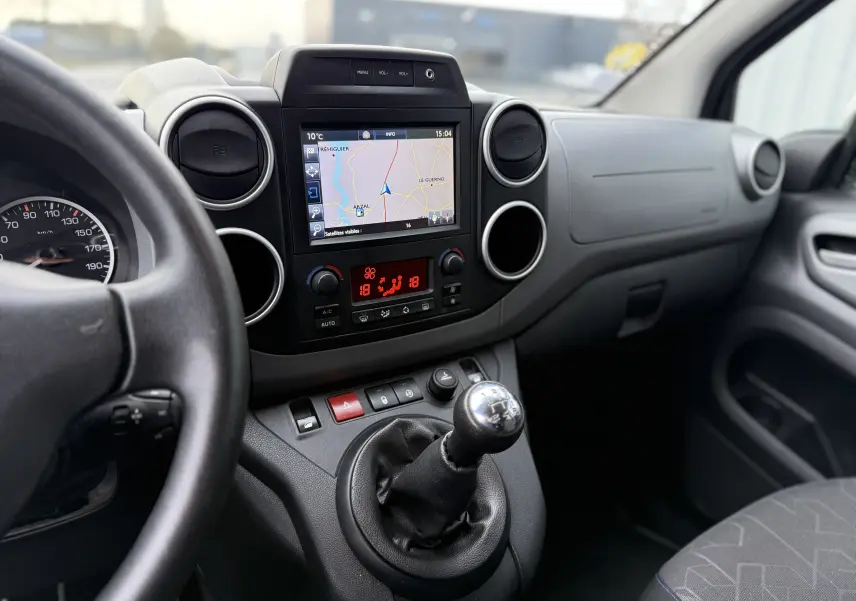 Vue intérieure centrée sur la console centrale et levier de vitesses manuelle du Peugeot Partner Tepee gris avec écran GPS et commandes climatisation.