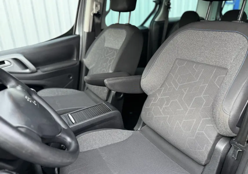 Intérieur du Peugeot Partner Tepee 2018, vue rapprochée des sièges avant en tissu gris avec accoudoirs et volant visible.