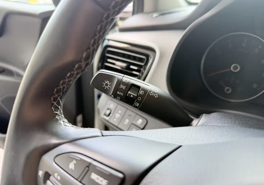 Gros plan sur la commande des phares à gauche du volant noir, avec tableau de bord flou du Kia Stonic blanc 2023.