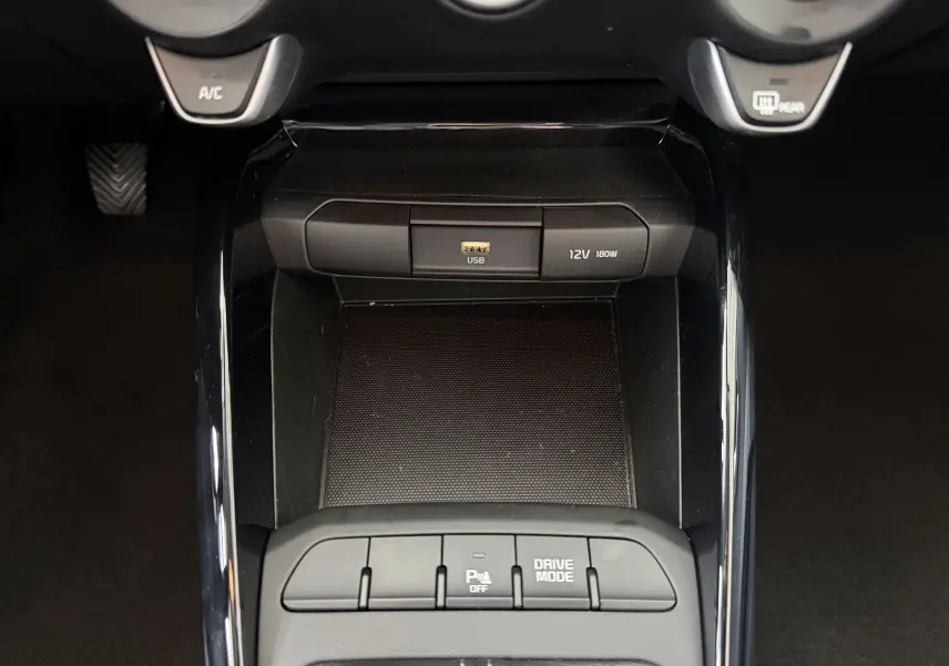 Vue rapprochée de la console centrale noire du Kia Stonic 2023, avec ports USB et 12V, boutons de mode de conduite et assistance parking.