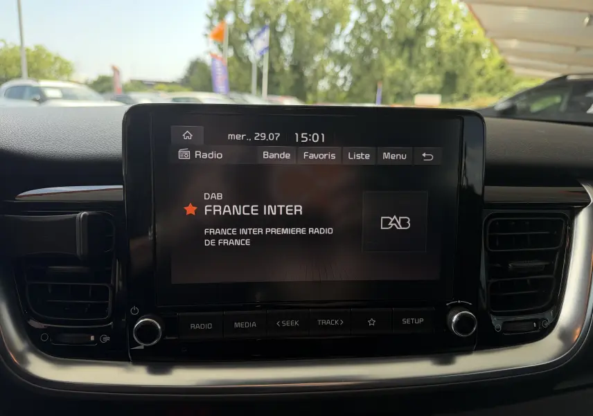 Écran central tactile du tableau de bord d'une KIA Stonic blanc, affichant la radio France Inter en mode DAB.