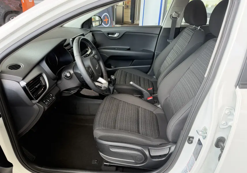 Intérieur de la KIA STONIC blanc, vue côté conducteur, montrant les sièges noirs et le volant multifonction.
