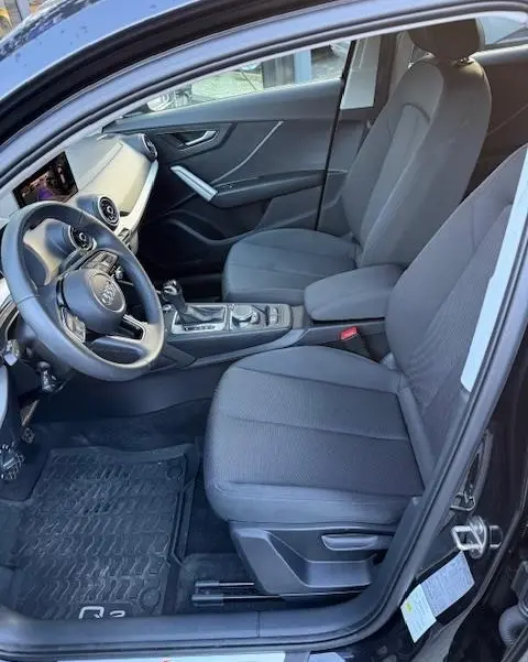 Vue intérieure côté conducteur de l'Audi Q2 noir 2023, sièges tissu gris, volant cuir multifonctions et console centrale visible.