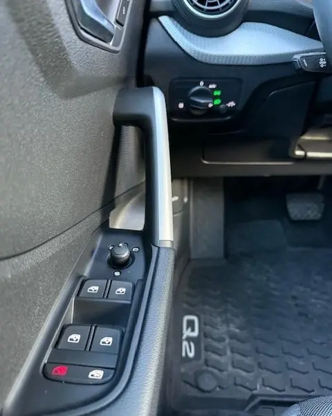 Gros plan sur la porte côté conducteur de l'Audi Q2 noire, montrant les commandes des vitres et le tapis de sol Q2.