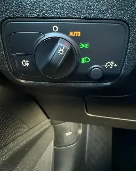 Gros plan sur la molette de commande des phares allumée en mode automatique dans un Audi Q2 noir 2023.