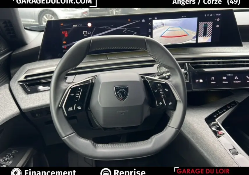 Vue intérieure centrée sur le volant du Peugeot 5008 bleu 2024 avec tableau de bord numérique et caméra de recul affichée.