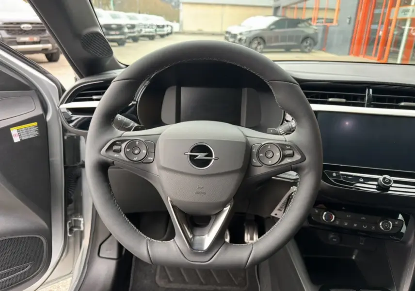 Vue intérieure centrée sur le volant cuir multifonctions d’une Opel Corsa gris kristall avec tableau de bord moderne.
