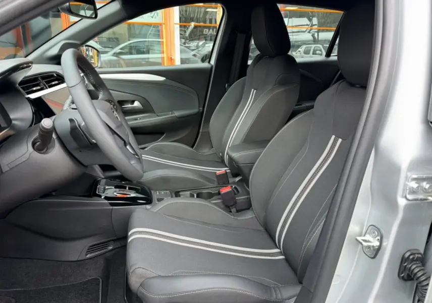 Vue intérieure côté conducteur de l’Opel Corsa gris kristall, sièges avant en tissu noir avec bandes blanches et volant multifonctions.