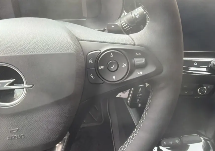 Gros plan sur le volant cuir multifonctions de l’Opel Corsa Hybrid 110 e-DCT6, avec commandes intégrées et logo Opel central.