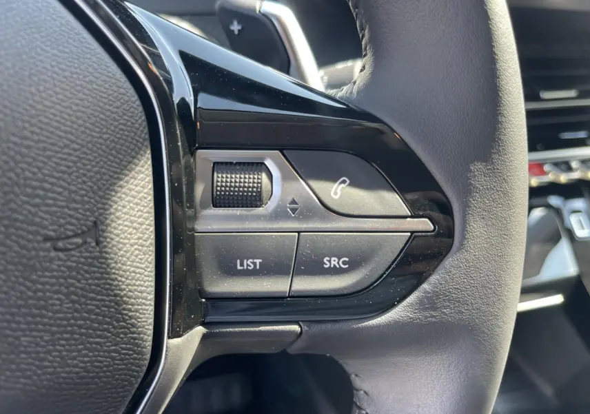 Gros plan sur les commandes gauche du volant cuir noir du Peugeot 208 New II 2024, avec boutons multifonctions.