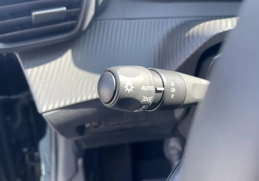 Gros plan sur la commande des feux automatique dans l'habitacle noir du Peugeot 208 New II 2024.
