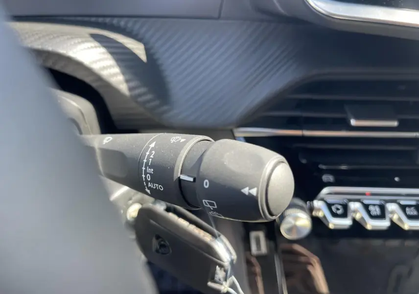 Gros plan sur la commande d'essuie-glace à gauche du volant dans l'habitacle noir du Peugeot 208 2024.