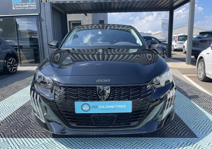 Vue frontale d'une Peugeot 208 noire Onyx avec calandre noire et feux LED 3 griffes, stationnée en extérieur.