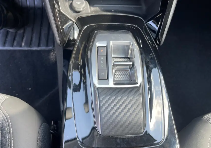 Vue rapprochée de la console centrale noire brillante avec sélecteur de boîte auto et surface effet carbone sur Peugeot 208 2024.