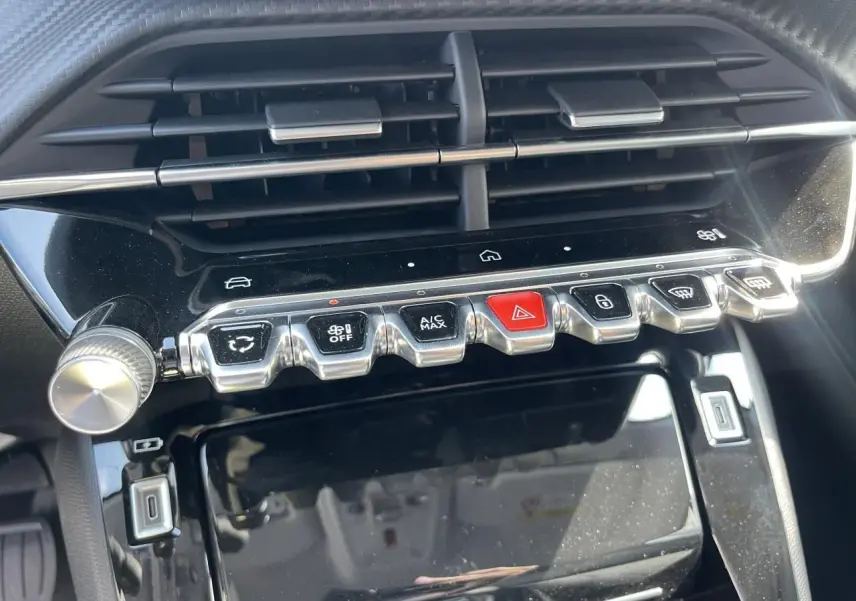 Vue rapprochée de la console centrale noire du Peugeot 208 2024 avec boutons chromés et écran tactile éteint.
