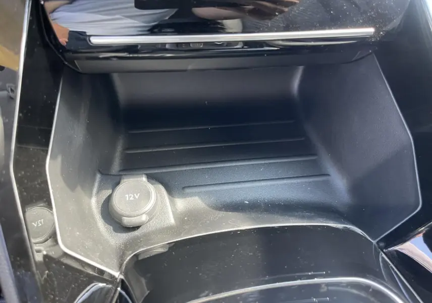 Prise 12V dans la console centrale noire brillante d'une Peugeot 208 noir Onyx, version 2024 vue en gros plan.