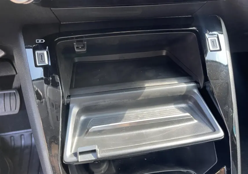 Gros plan sur la console centrale noire brillante de la Peugeot 208 2024 avec compartiment ouvert et prises USB visibles.