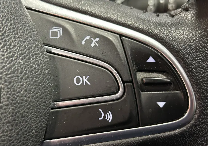 Gros plan sur les commandes au volant noir du Renault Kadjar gris, avec boutons OK, téléphone et volume sonore.