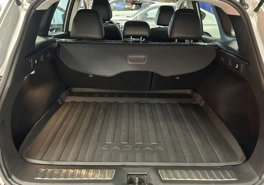 Coffre ouvert d’un Renault Kadjar gris, vue arrière montrant la protection de coffre et les sièges arrière noirs.