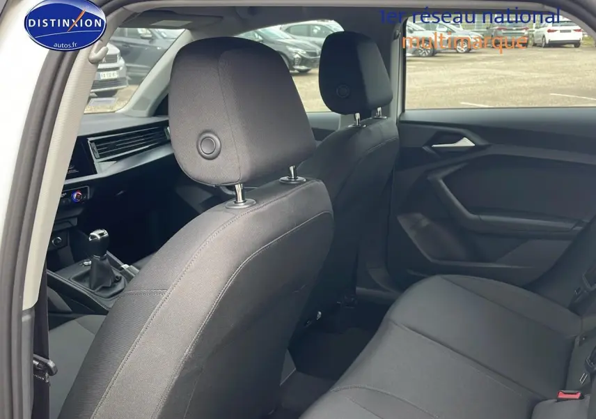 Vue intérieure arrière de l'Audi A1 Sportback 2022 blanche, montrant les sièges noirs et la boîte manuelle côté gauche.