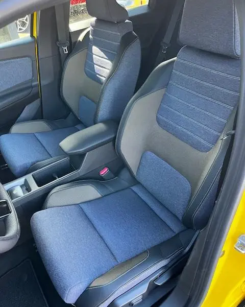 Vue intérieure côté avant droit de la Renault R5 Techno 150 ch 2024 jaune, sièges tissu bleu et gris avec accoudoir central.