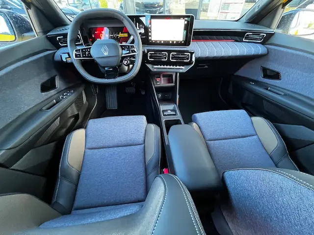 Vue intérieure avant de la Renault R5 Techno 150 ch 2024, montrant le tableau de bord avec écran tactile central et sièges tissu gris.