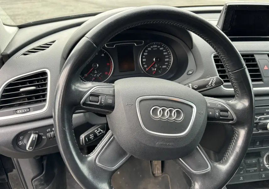 Vue rapprochée du volant noir d'un Audi Q3 2014 avec tableau de bord et commandes intégrées visibles.