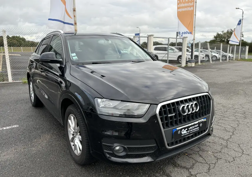 Audi Q3 noir vue 3/4 avant droit sur parking, calandre chromée et phares LED distinctifs visibles.