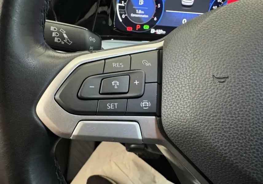 Gros plan sur les commandes au volant cuir noir d'une Volkswagen Golf 2.0 TDI 2021, avec tableau de bord numérique visible.