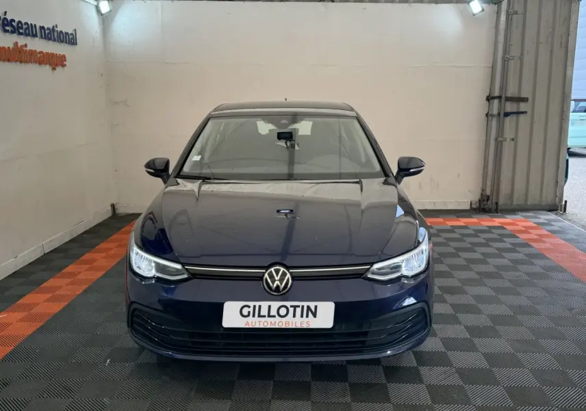 Vue frontale d'une Volkswagen Golf bleu foncé garée dans un garage avec plaque GILLOTIN visible.