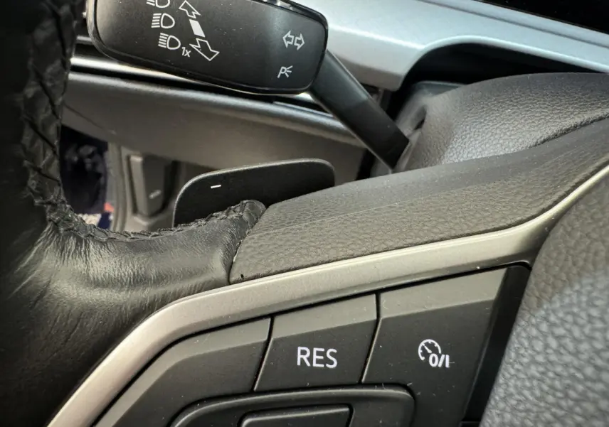 Gros plan sur les commandes au volant cuir noir de la Volkswagen Golf bleue, avec bouton régulateur de vitesse visible.