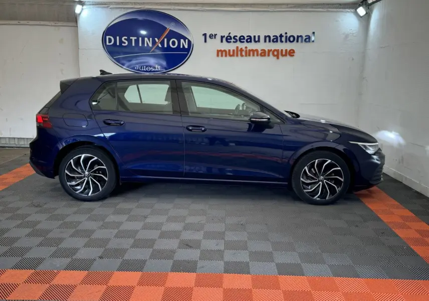Profil côté gauche d'une Volkswagen Golf 2.0 TDI bleu foncé dans un showroom avec sol à damier gris et orange.
