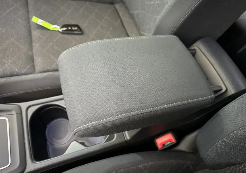 Gros plan sur l'accoudoir central noir et la console entre les sièges avant d'une Volkswagen Golf bleue.