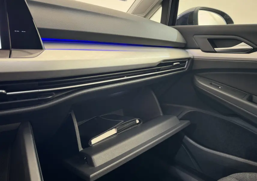 Intérieur côté passager de la Volkswagen Golf 2.0 TDI bleu, tableau de bord avec éclairage bleu et boîte à gants ouverte.