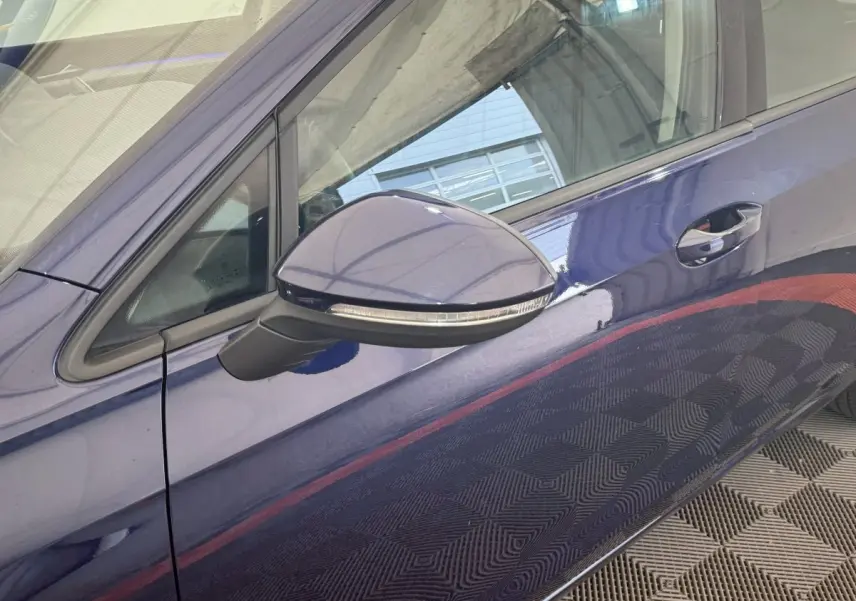 Vue rapprochée du rétroviseur côté gauche d'une Volkswagen Golf bleu métallisé 2021 avec poignée de porte visible.
