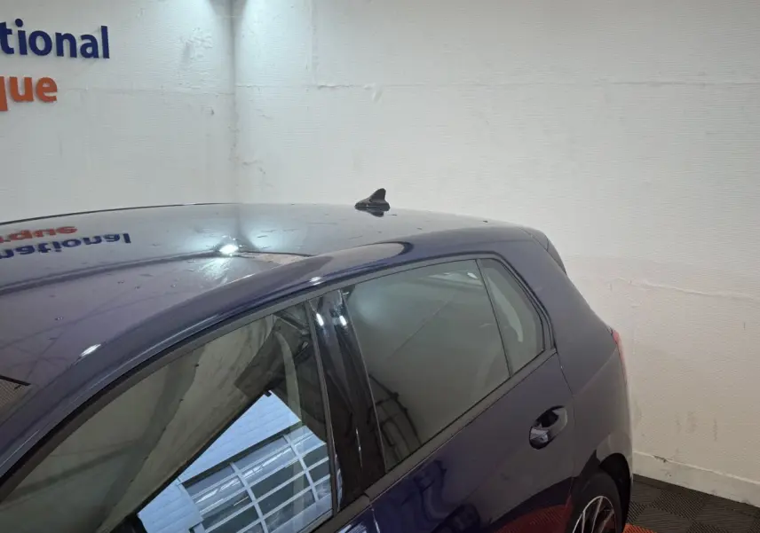 Vue 3/4 arrière droite d'une Volkswagen Golf bleu métallisé garée en intérieur, avec antenne requin sur le toit.